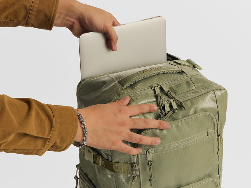 Model putting in laptop in the Terra 26L Laptop Duffel Backpack in green Juniper
