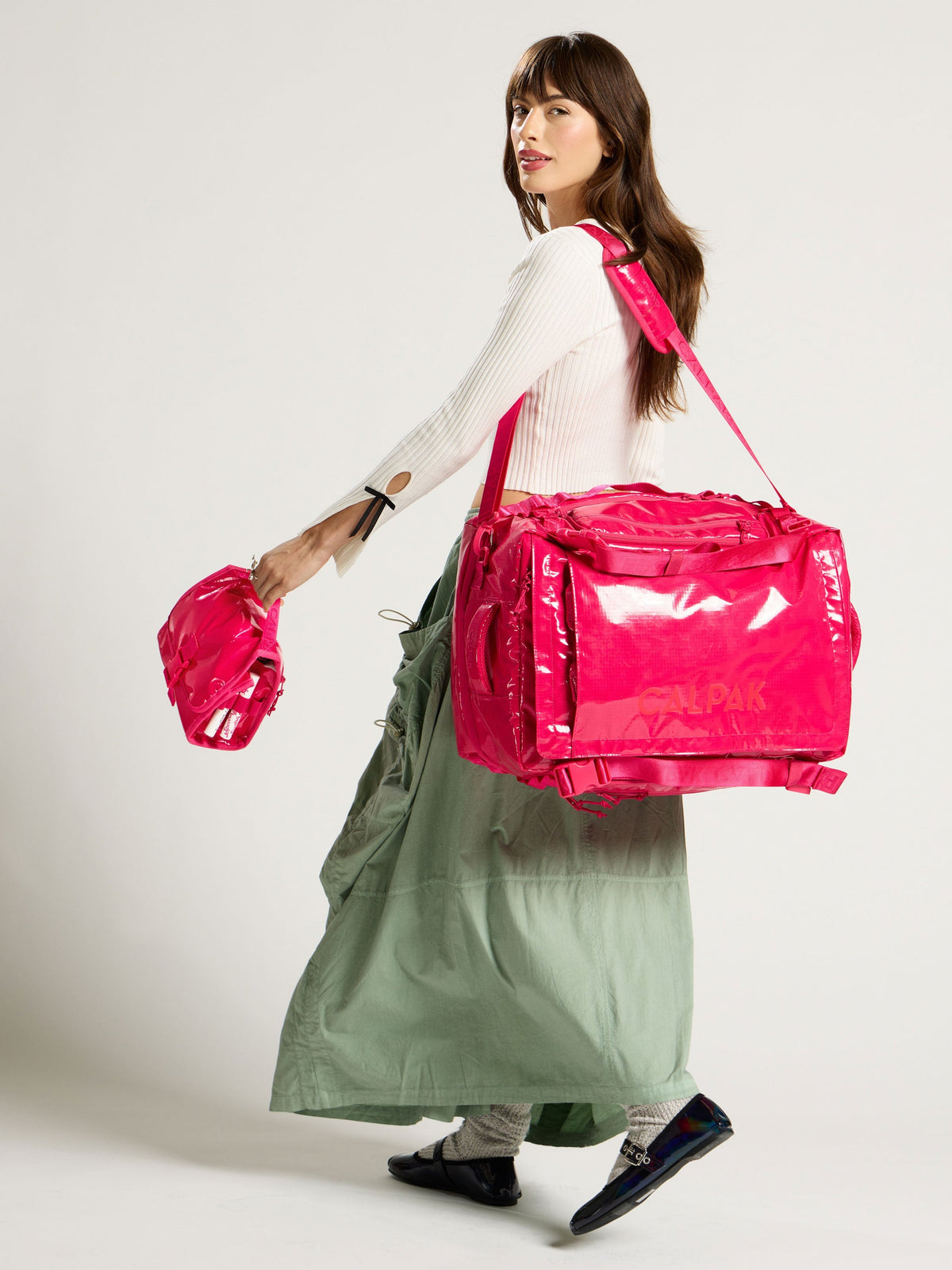 Model holding dragonfruit CALPAK Terra Hanging Toiletry Bag with Terra 50L Backpack Duffel over shoulder; THY2201-DRAGONFRUIT