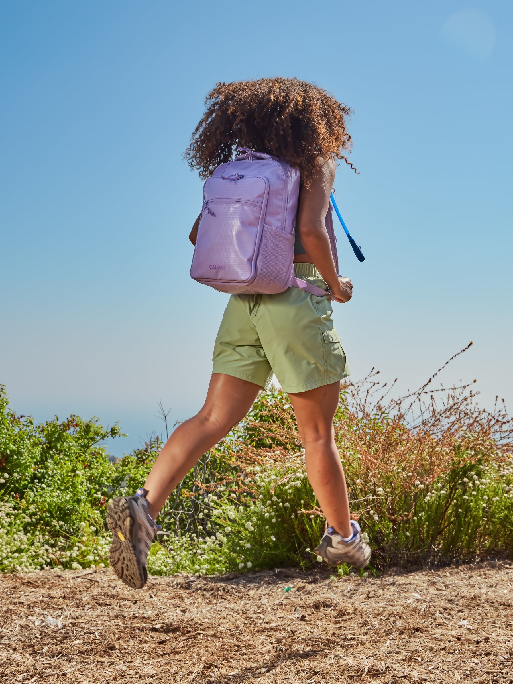 Model hiking while wearing CALPAK Terra Hydration Backpack in light purple