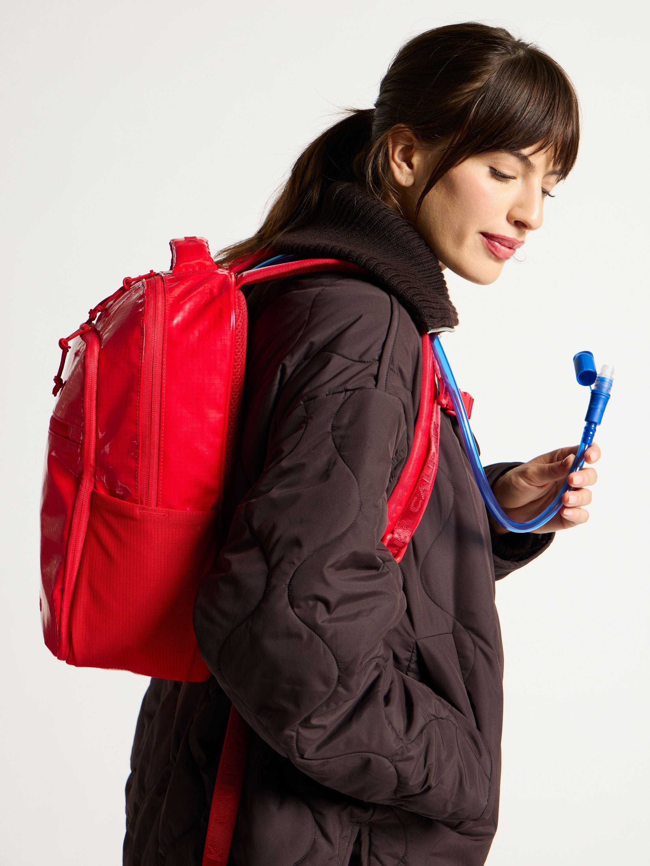 Model showing straw of removable hydration reservoir within red CALPAK Terra Hydration Backpack