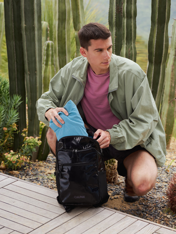 Model packing items in his black CALPAK hydration backpack