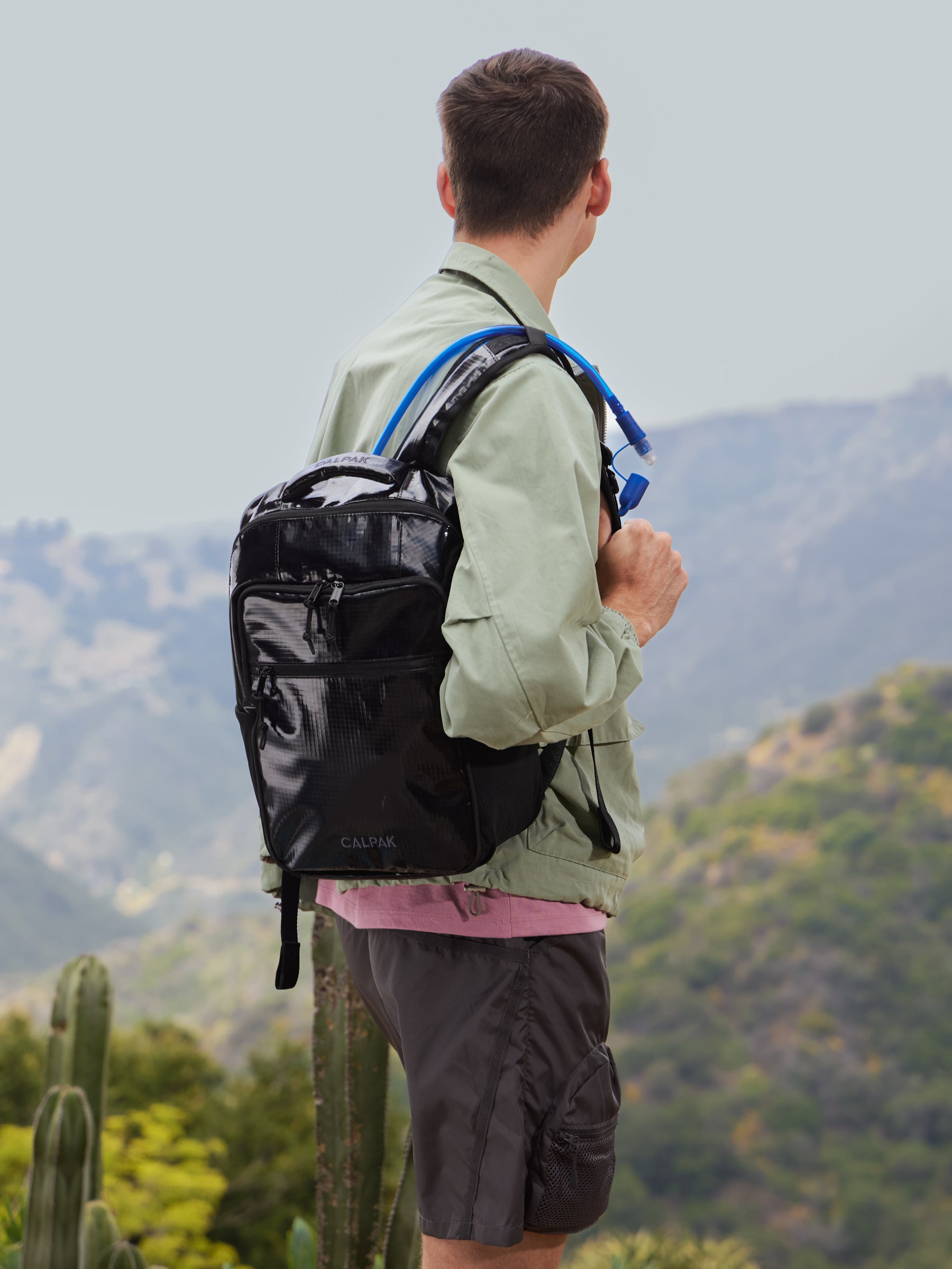 Model looking out to the distance while wearing CALPAK Terra Hydration Backpack with removable hydration pack straw in obsidian