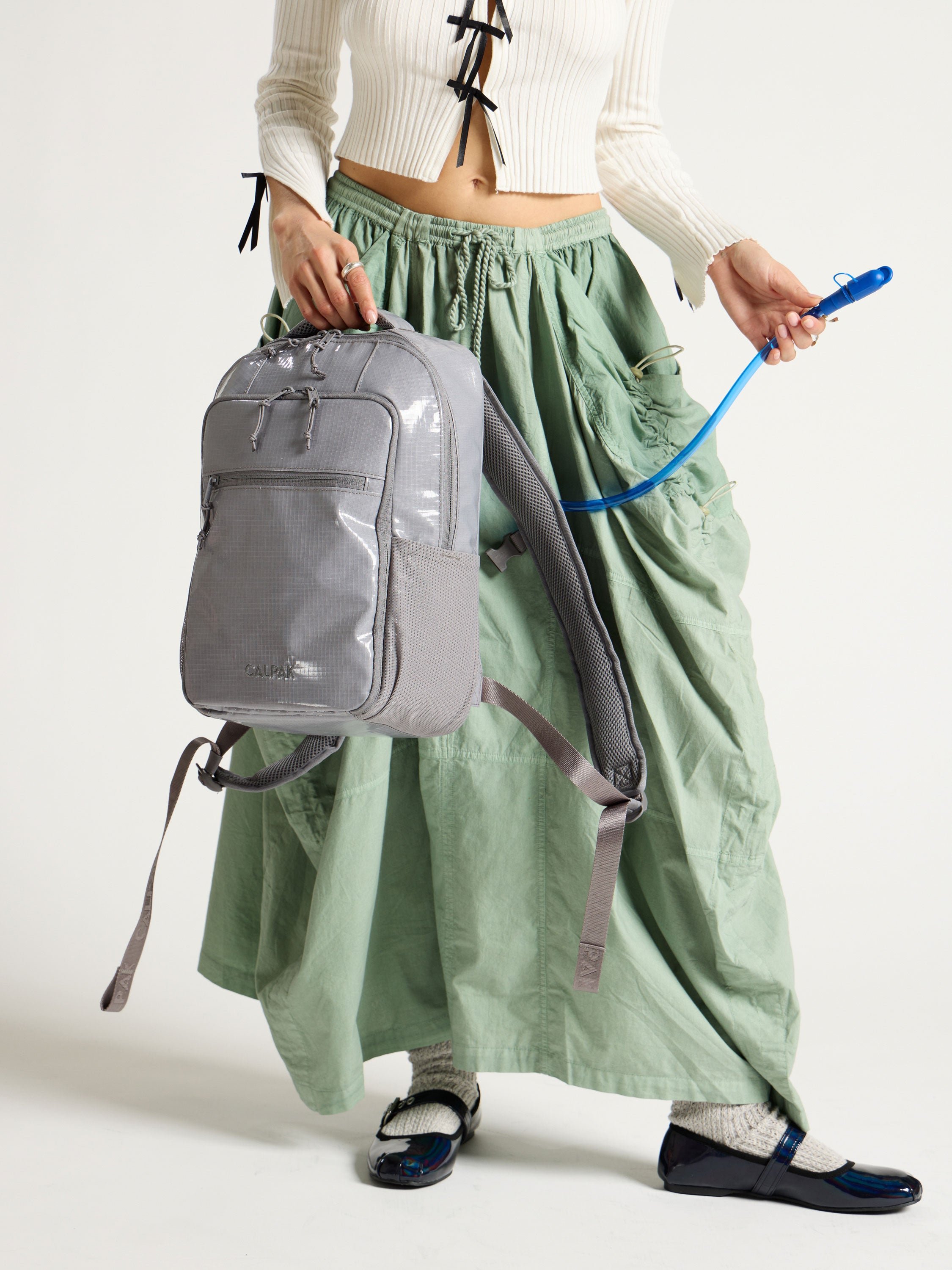 Model displaying straw of removable hydration reservoir in gray CALPAK Terra Hydration Backpack