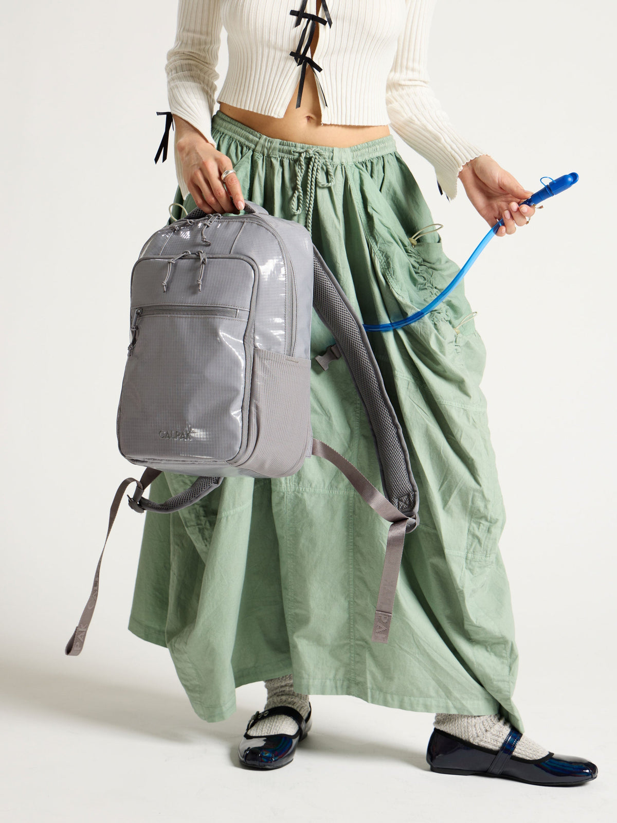 Model displaying straw of removable hydration reservoir in gray CALPAK Terra Hydration Backpack; BPT2201-STORM