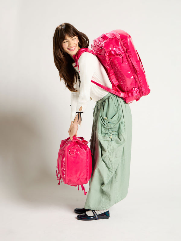 Model wearing Terra Large 50L Duffel Backpack on back with Terra 26L Laptop Duffel Backpack in hands in dragonfruit