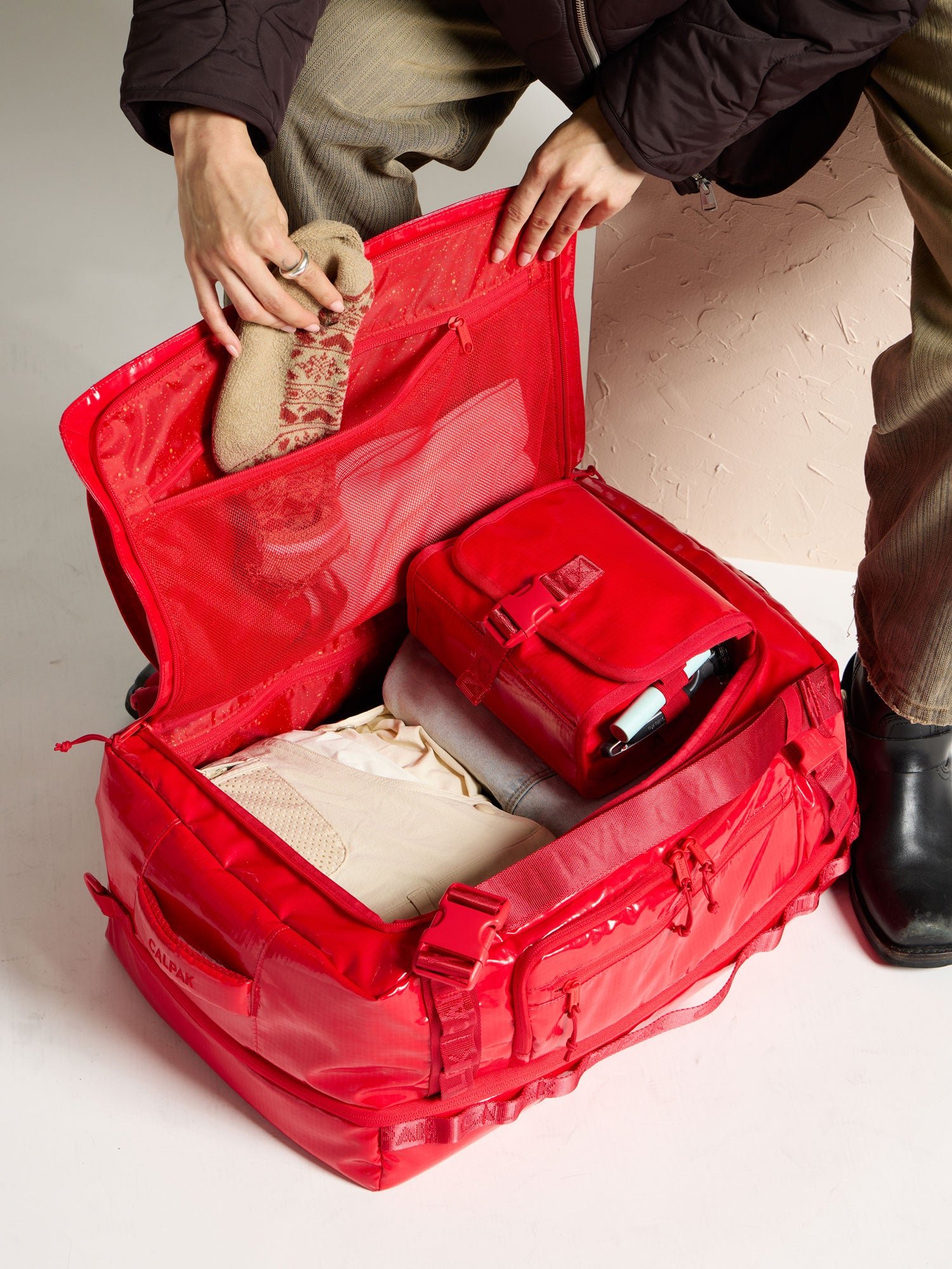 Model placing socks into mesh interior pocket of Terra Large 50L Duffel Backpack in red; DTL2301-FLAME