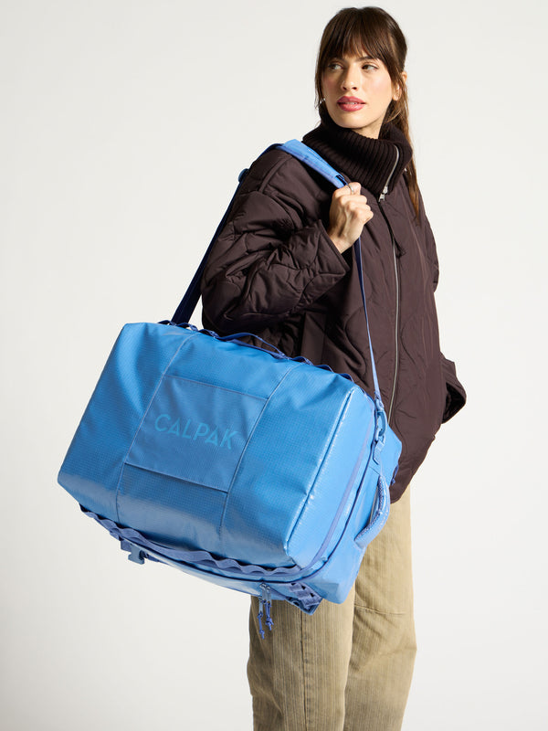 Model wearing crossbody strap of blue terra large 50L duffel backpack over shoulder