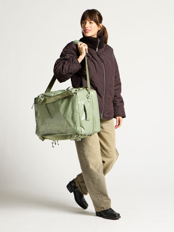 Model using adjustable shoulder strap to hold green terra large 50L duffel backpack as duffel bag