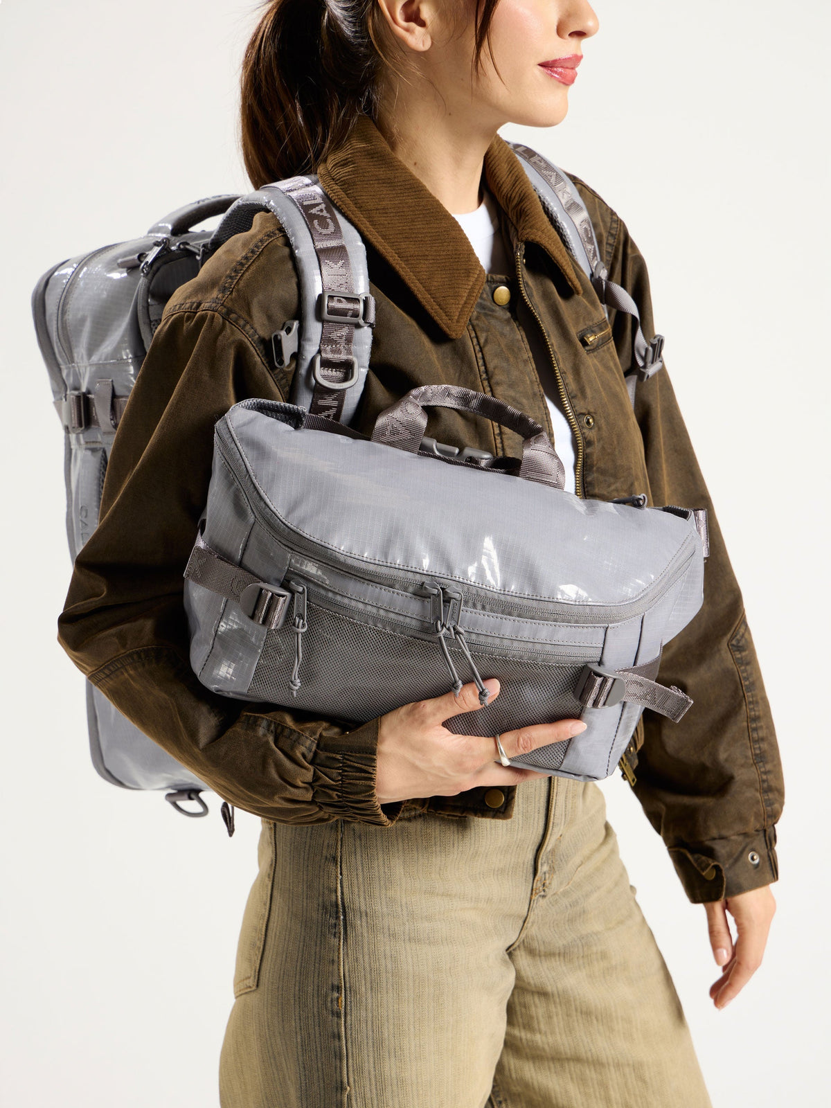 Model wearing CALPAK Terra 26L Laptop Backpack Duffel while holding gray Terra Sling Bag in arm; CBH2201-STORM
