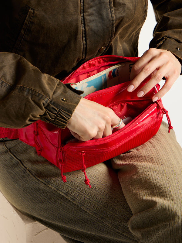 Model placing items interior of red CALPAK Terra Small Sling Bag