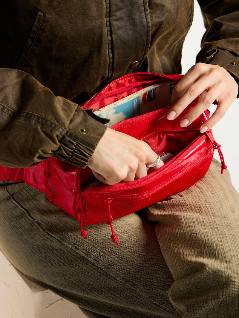 Model placing items interior of red CALPAK Terra Small Sling Bag