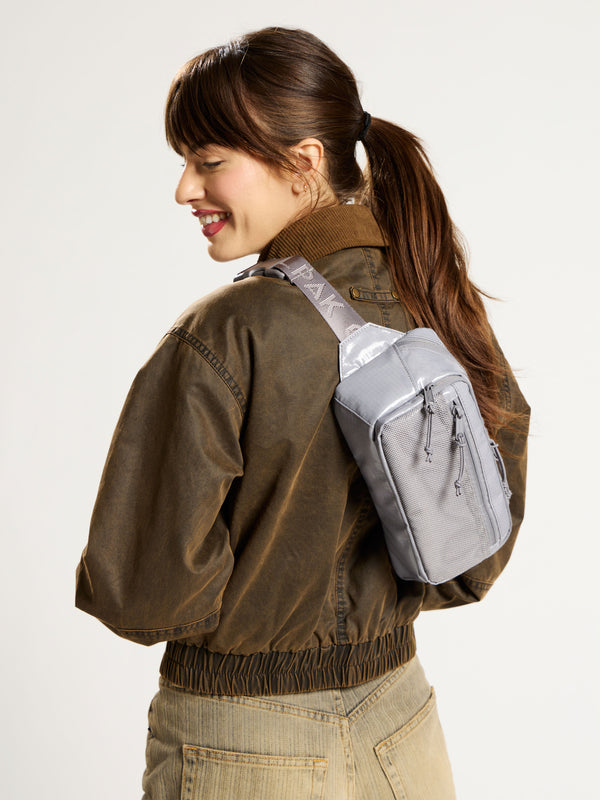 Model wearing gray CALPAK Terra Small Sling Bag as crossbody bag