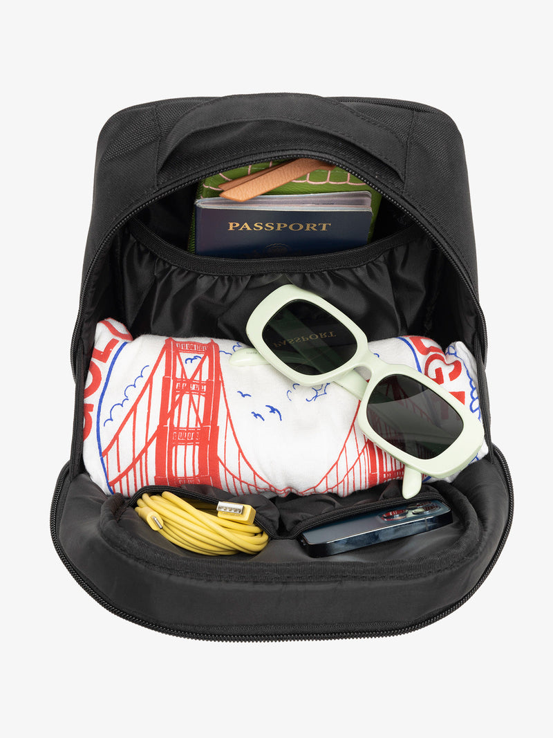 Interior view of black CALPAK The Everything Cube with notebook and passport in large slip pocket, cords and phone in front slip pockets, and sunglasses and t-shirt in main compartment