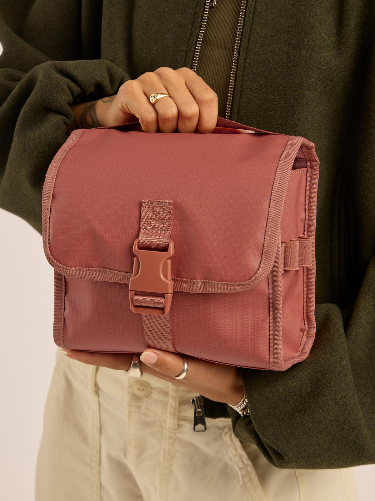 Model holding the CALPAK Terra Hanging Toiletry Bag in red and orange Matte Clay; THY2201-CLAY