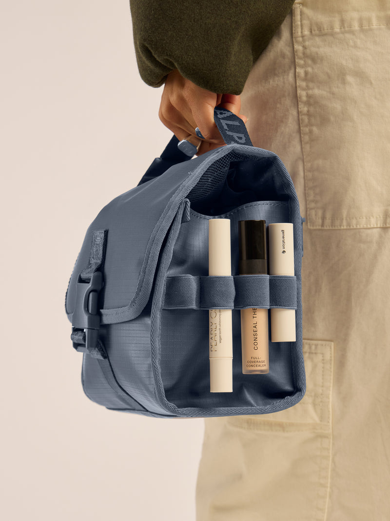 Model holding the CALPAK Terra Hanging Toiletry Bag in blue Matte Indigo; THY2201-INDIGO