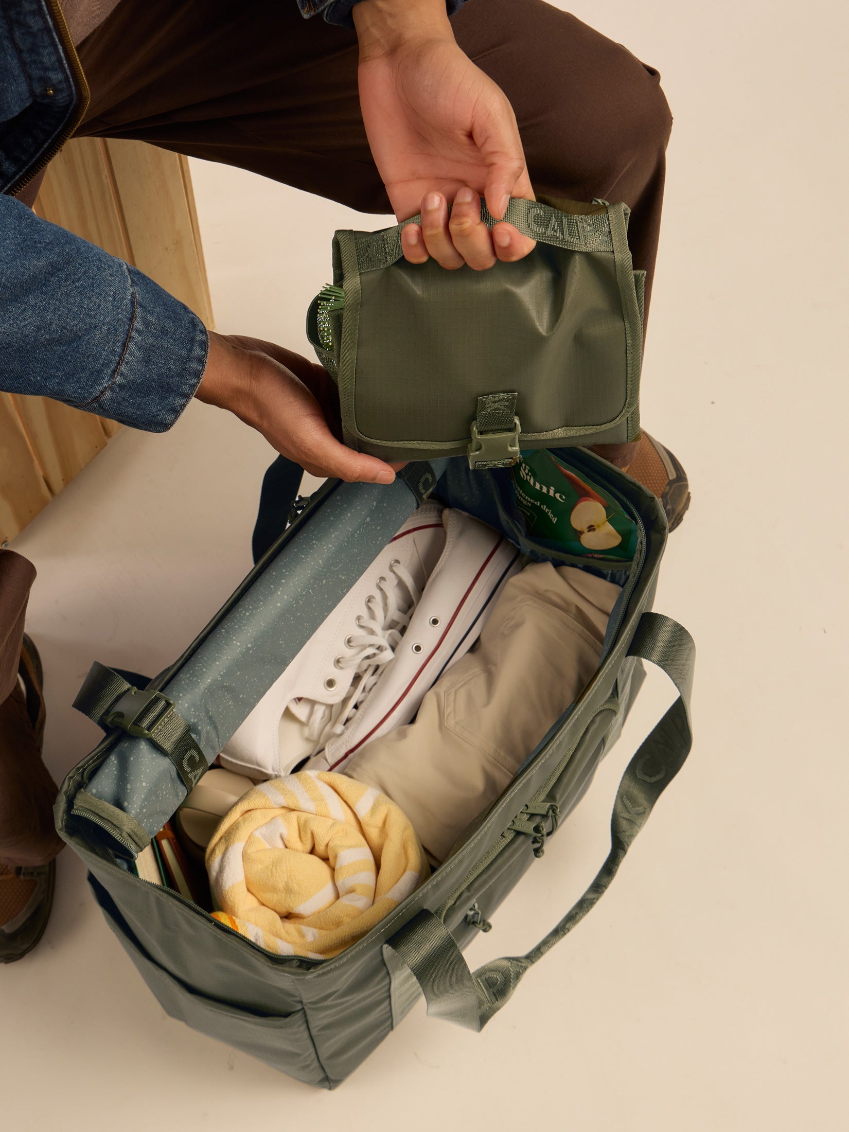 Model packing the CALPAK Terra Hanging Toiletry Bag in dark green Matte Pine; THY2201-PINE