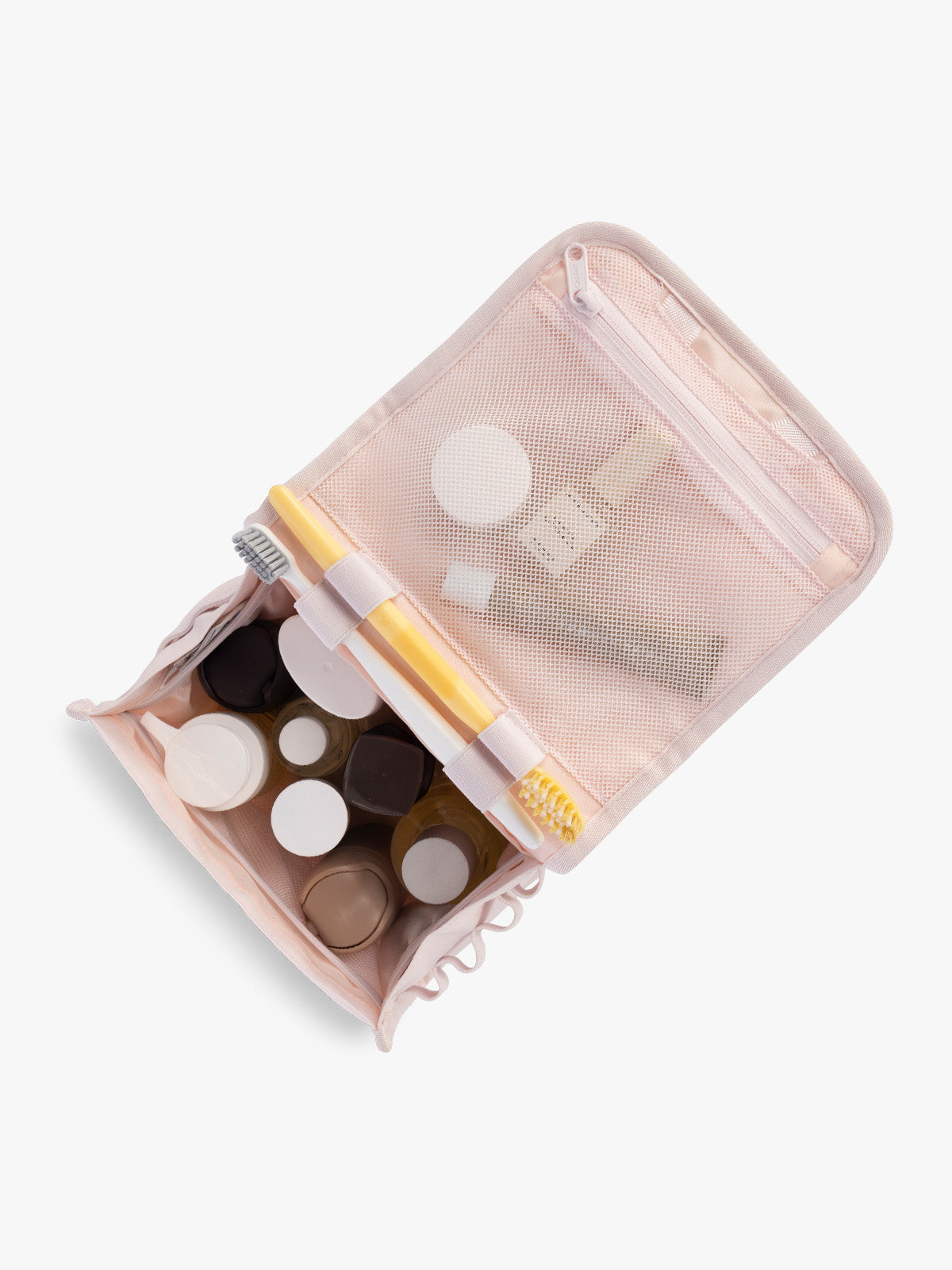 Toiletry items in the CALPAK Terra Hanging Toiletry Bag in light pink Shell Pink with front buckle; THY2201-SHELL-PINK