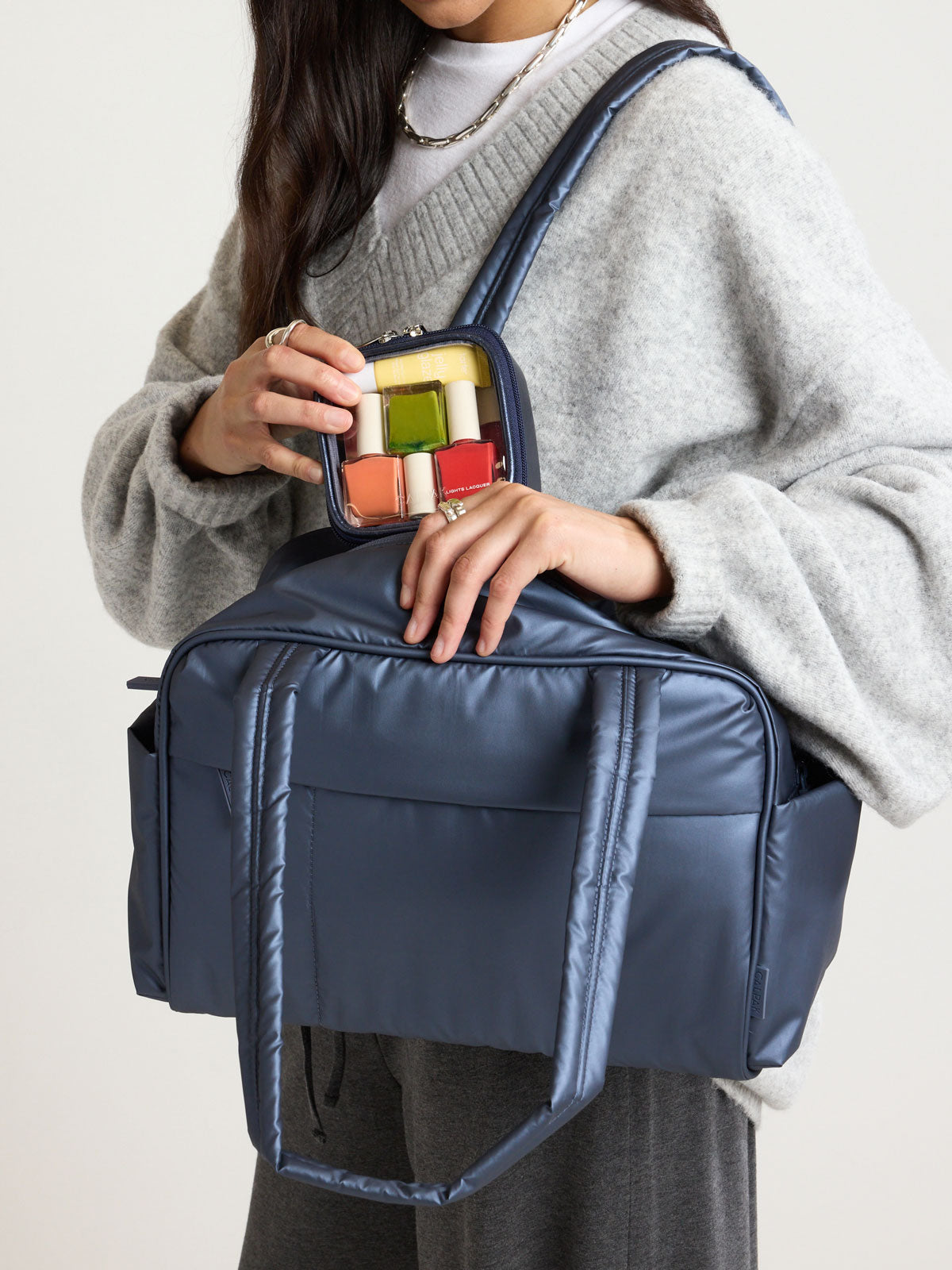 Person holding the CALPAK Clear Cosmetic Case in dark blue Metallic Indigo ; CCT2501-METALLIC-INDIGO