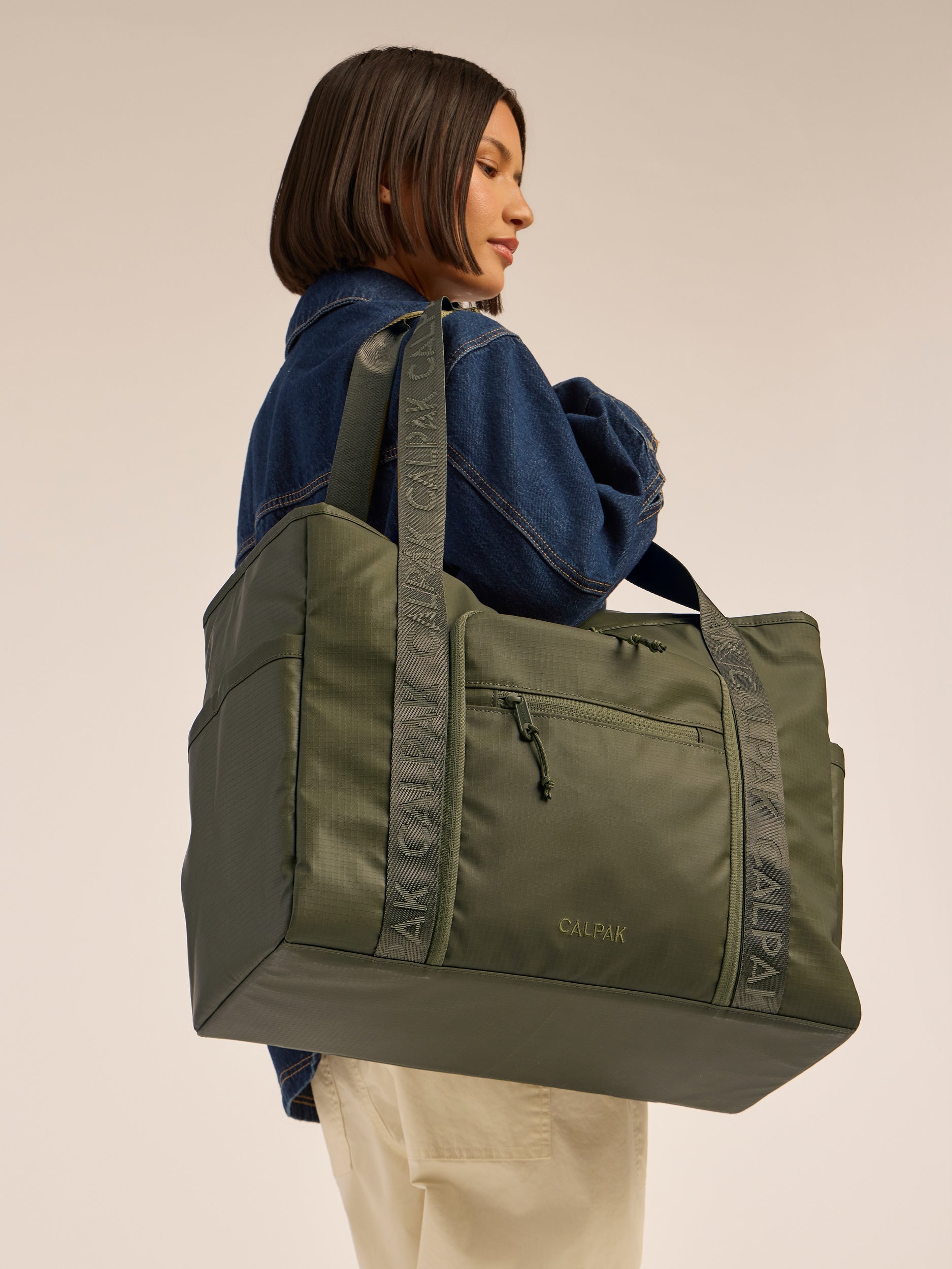 Model wearing the CALPAK Terra 35L Water Resistant Zippered Tote Bag in dark green Matte Pine; TTO2401-PINE