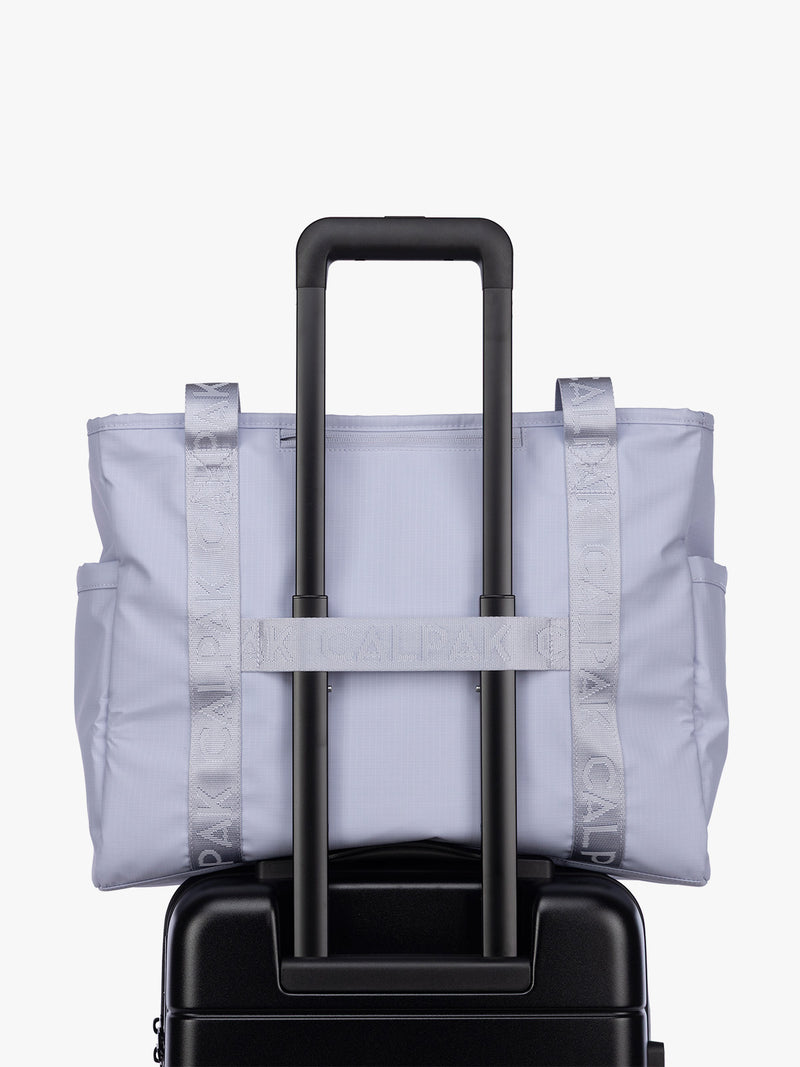 Luggage trolley strap of the CALPAK Terra 35L Tote Bag with multiple pockets and shoulder straps in shiny light lavender Sea Glass on a white background