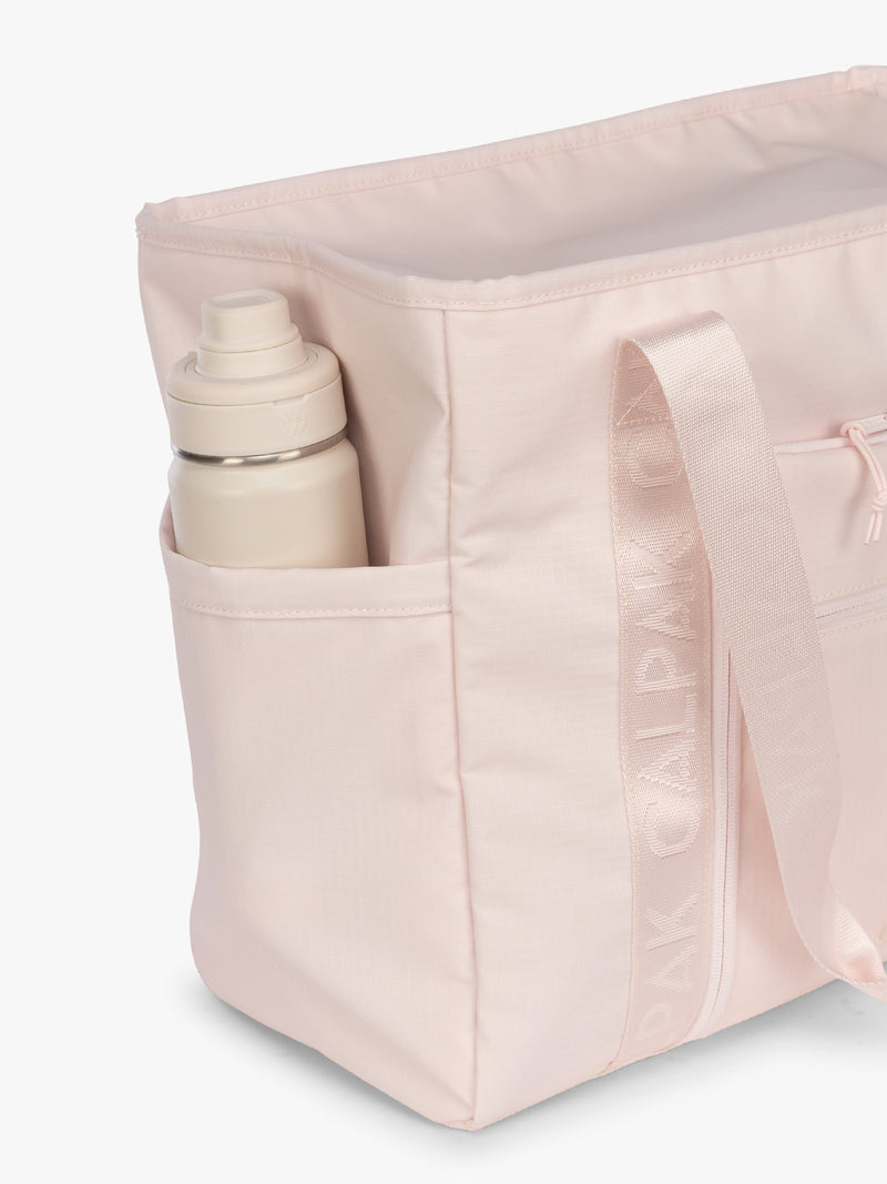 Side water bottle compartment pocket of the CALPAK Terra 35L Tote Bag with multiple pockets and shoulder straps in shiny light pink Shell Pink on a white background