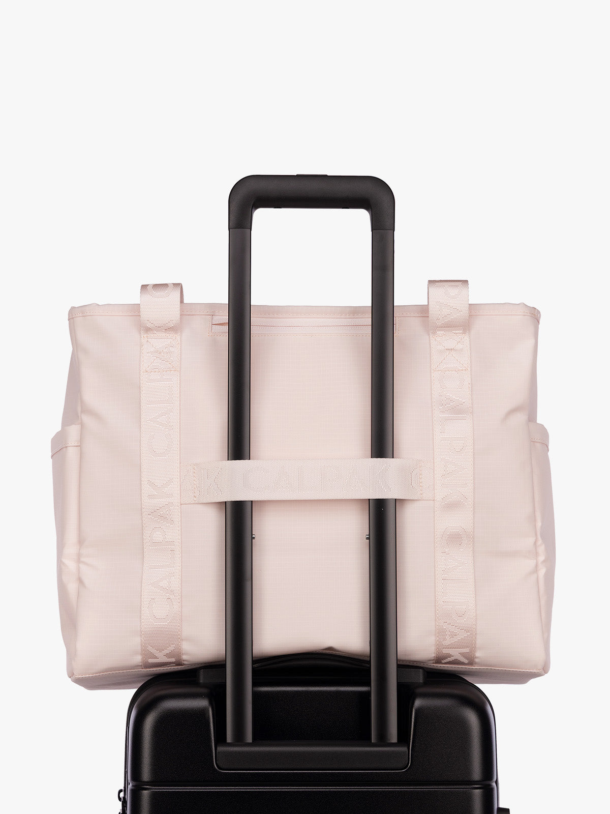 Luggage trolley strap of the CALPAK Terra 35L Tote Bag with multiple pockets and shoulder straps in shiny light pink Shell Pink on a white background; TTO2401-SHELL-PINK