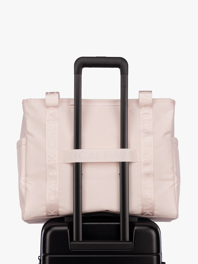 Luggage trolley strap of the CALPAK Terra 35L Tote Bag with multiple pockets and shoulder straps in shiny light pink Shell Pink on a white background