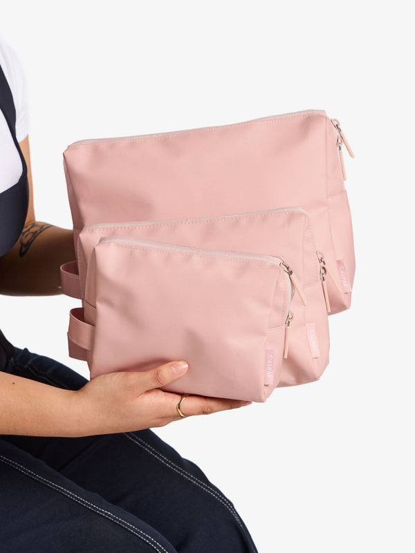 Model displaying the waterproof zippered pouch set in small, medium and large in pink