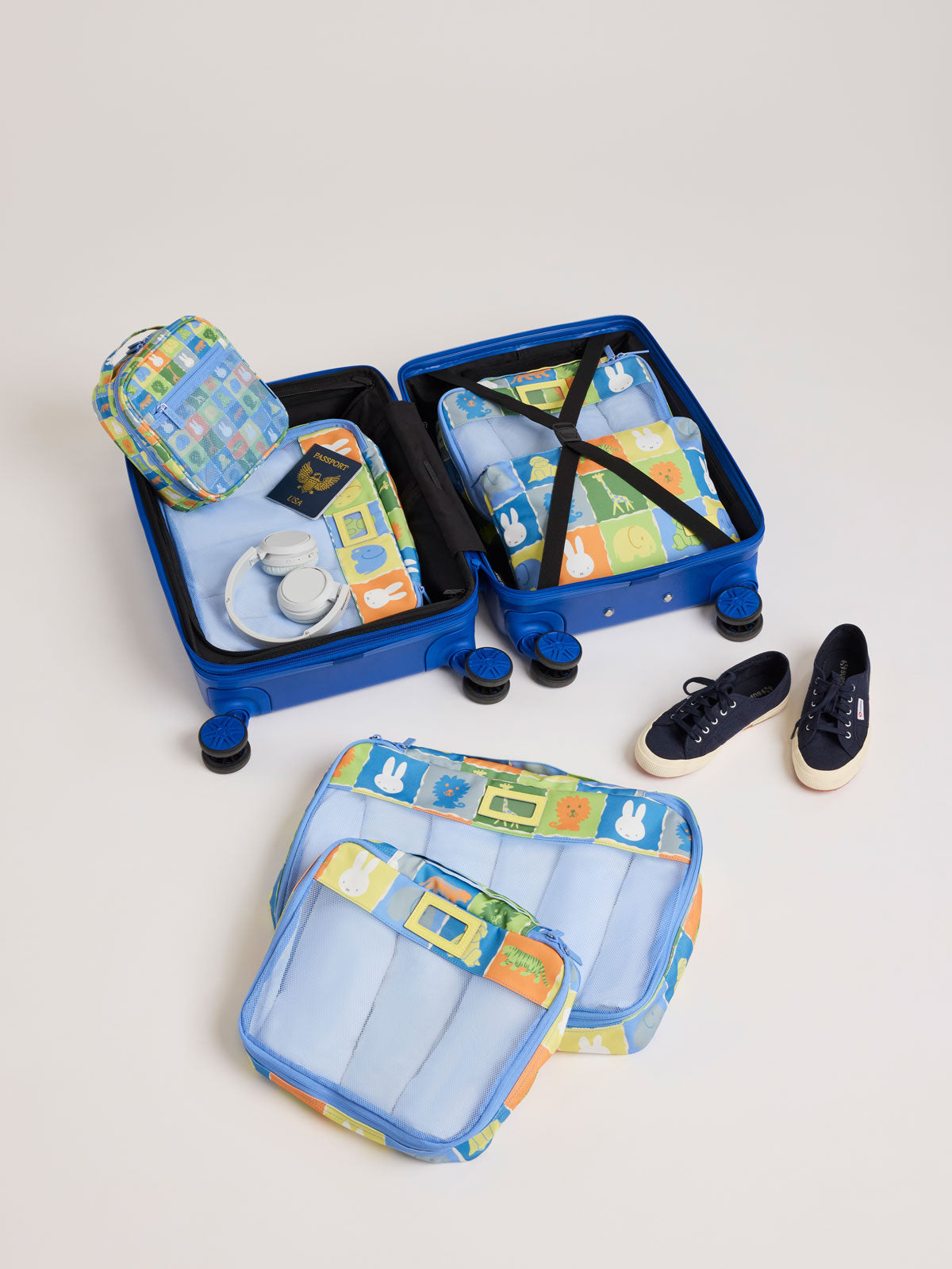 Colorful travel set of CALPAK Packing Cubes in colorful blue pouches with Miffy and animal pattern on a white background including a suitcase, shoes, and a bag on a light gray background; PC1601-MIFFY-BLUE-ZOO-TRIP