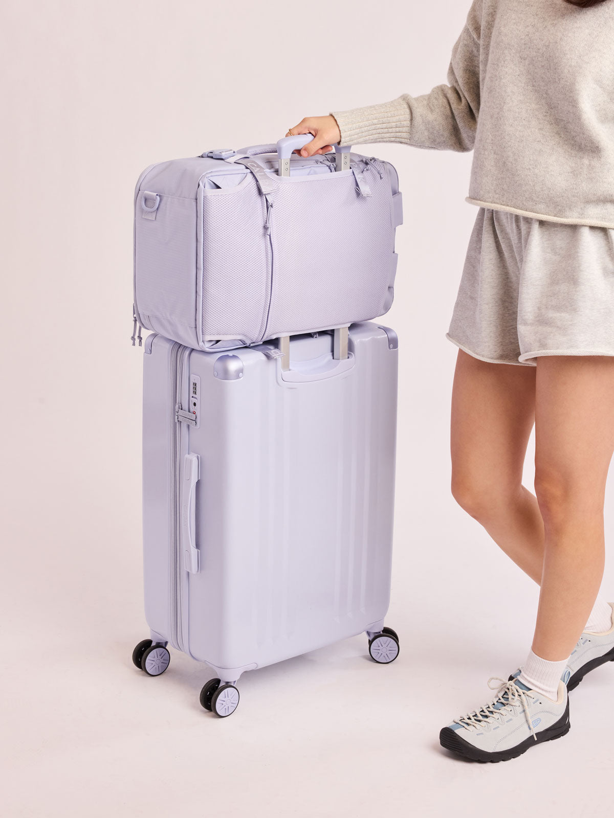 Model with CALPAK Ambeur Medium Luggage in light lavender purple in Sea Glass with handles and spinner wheels on a white background; LAM1024-SEA-GLASS