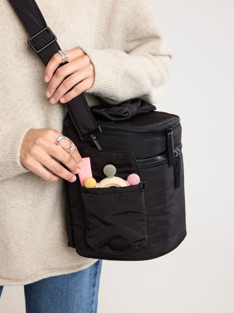 Woman putting items in the side pocket of CALPAK Insulated Baby Bottle Bag in Black