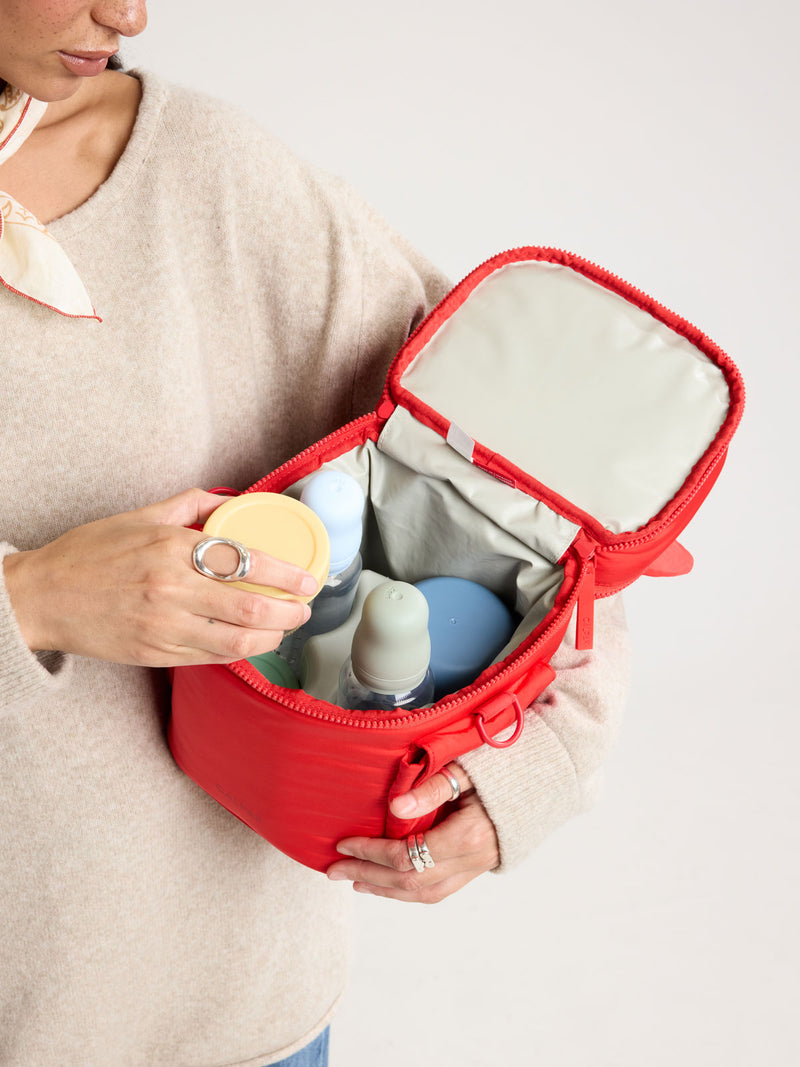 Person adding baby bottle in the CALPAK Insulated Baby Bottle Bag in red Tomato