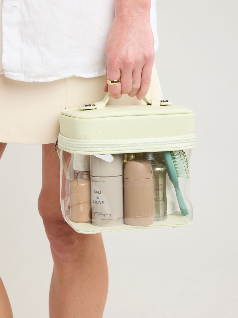 Person carrying CALPAK Clear Train Case in light green Celadon