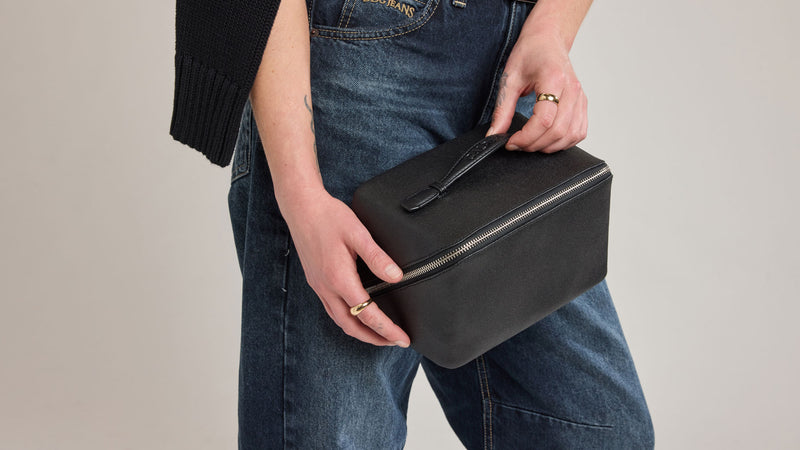 Person holding a black leather Canvas Colette Black Toiletry bag against a neutral background