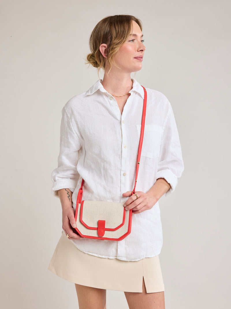 Woman wearing CALPAK Colette Canvas Crossbody Wallet Bag in Natural Brown with beige canvas material and red finishing
