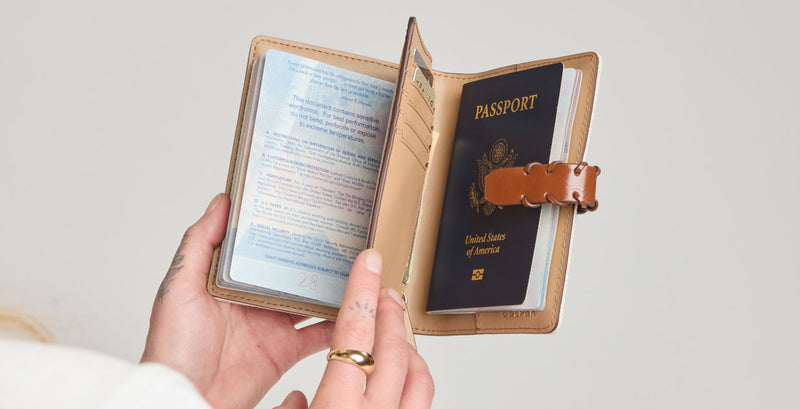 Person holding a CALPAK Colette Colette Passport Wallet with a passport inside on a light gray background