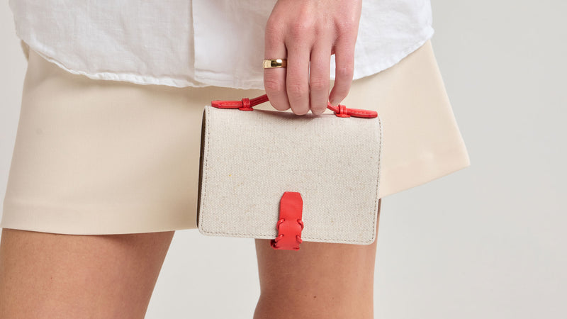 Person holding a beige Colette Multi Passport Canvas Wallet with red accents against a neutral background
