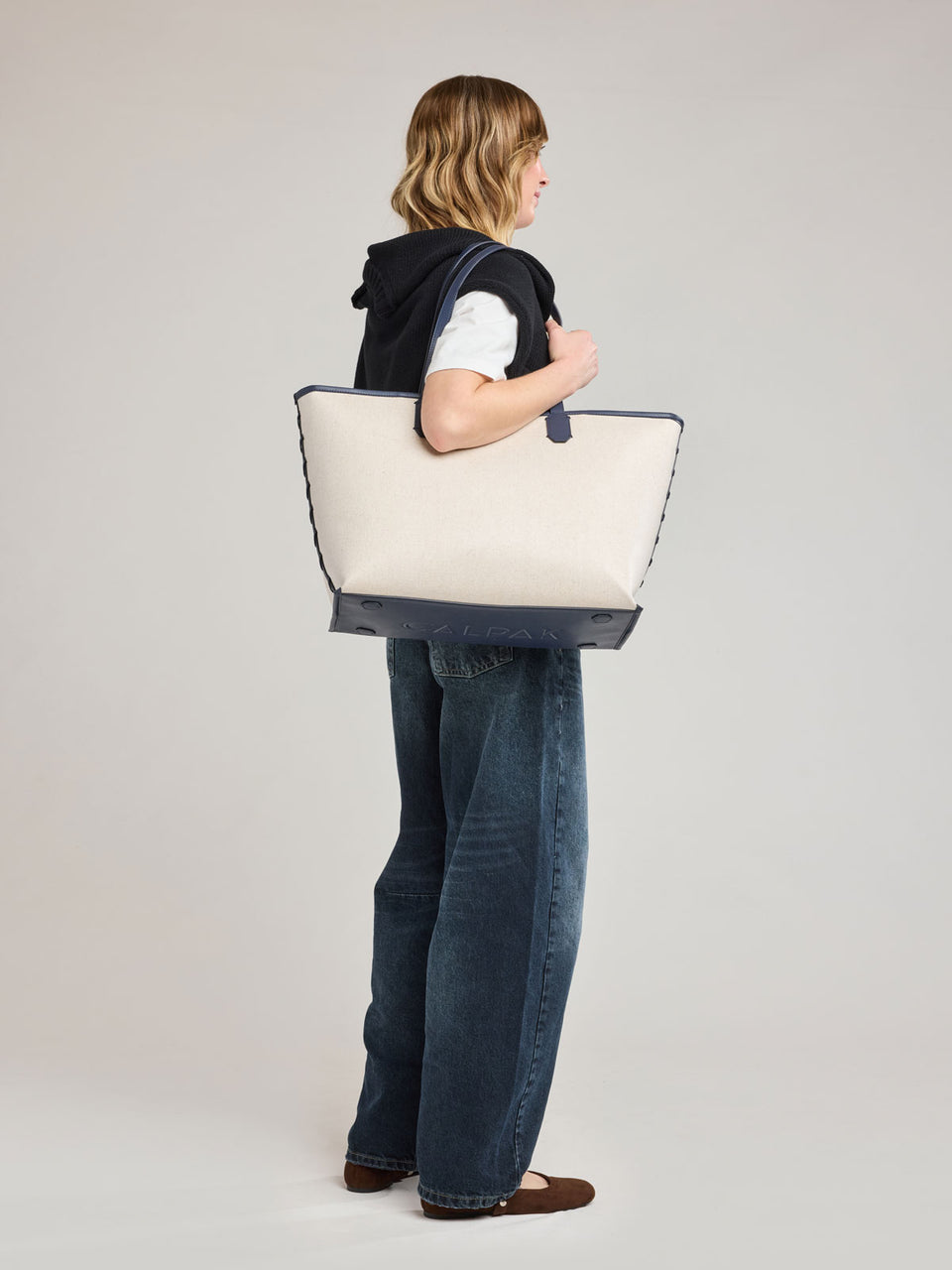 Woman wearing CALPAK Colette 15" Canvas Laptop Tote in beige canvas material  with blue finishing in Natural Navy; CLCT2601-NATURAL-NAVY