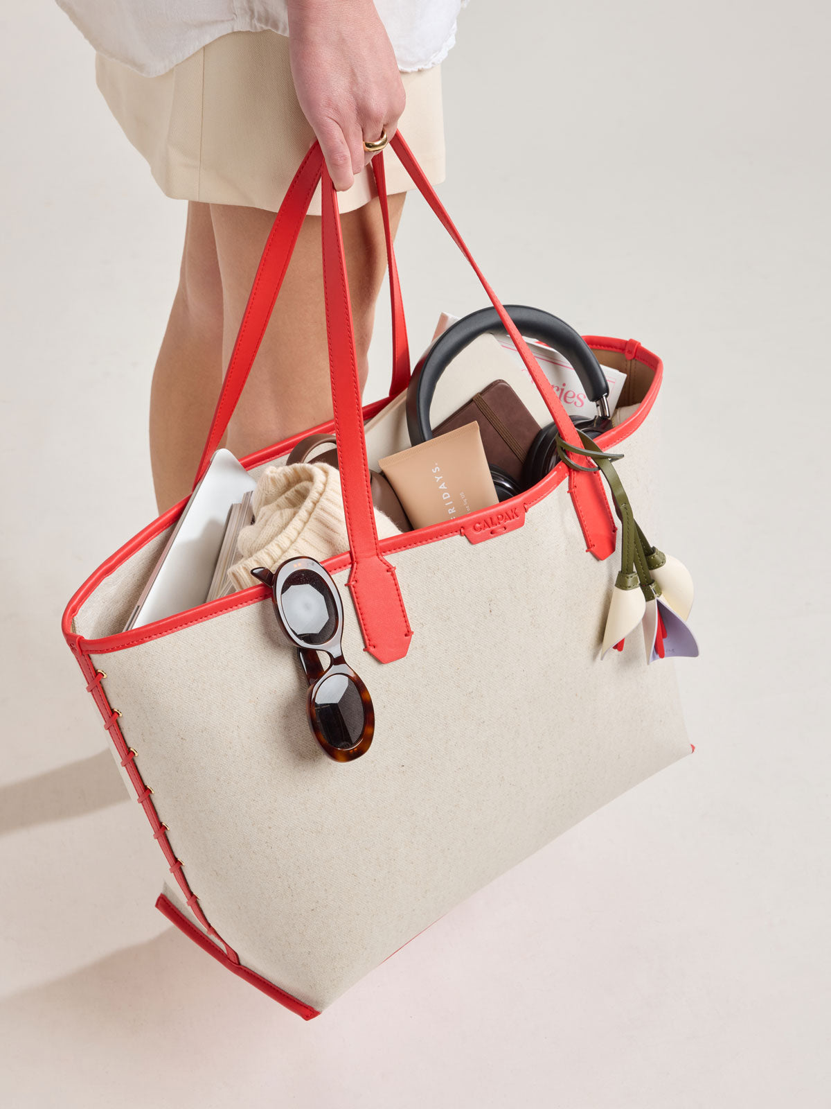Model holding CALPAK Colette 15" Canvas Laptop Tote in beige canvas material  with red finishing in Natural Tomato; CLCT2601-NATURAL-TOMATO