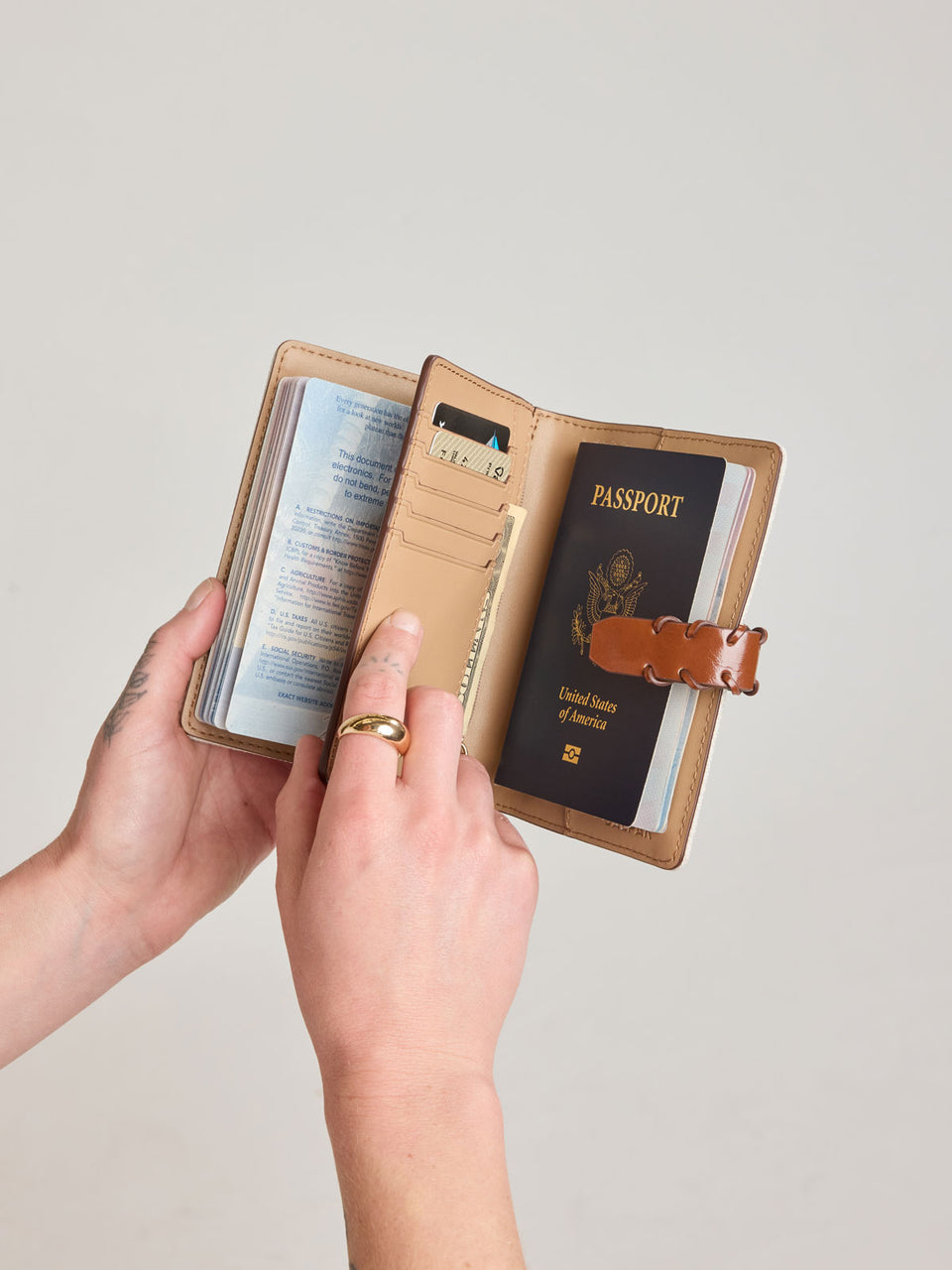 Model opening CALPAK Colette Multi Passport Wallet in beige canvas material and brown finishings in Natural Brown; CLPW2601-NATURAL-BROWN