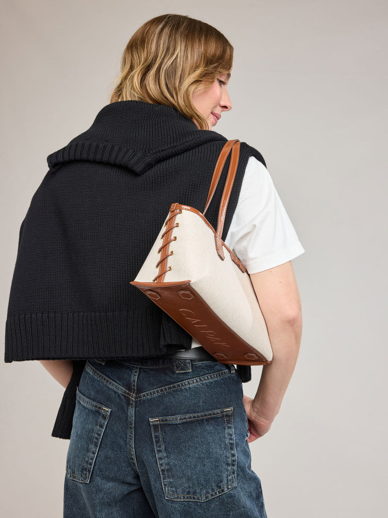 Woman wearing CALPAK Colette Canvas Shoulder Tote in beige canvas material and brown finishing