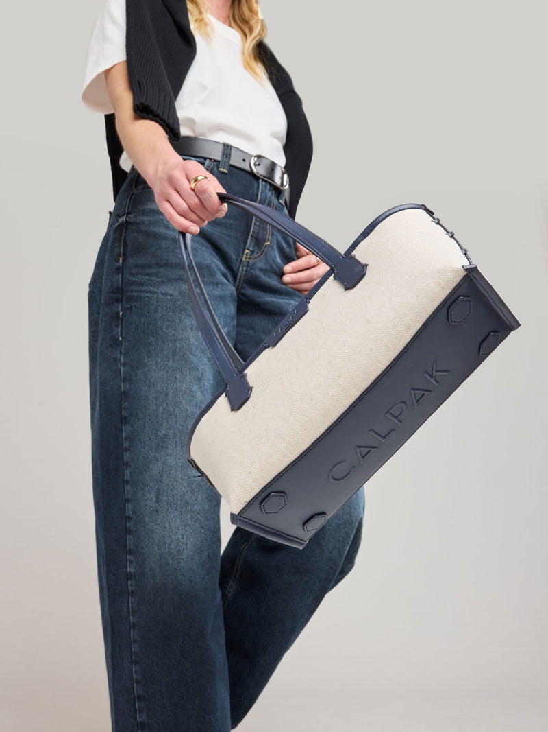 Woman holding CALPAK Colette Canvas Shoulder Tote in beige canvas material  and blue finishing