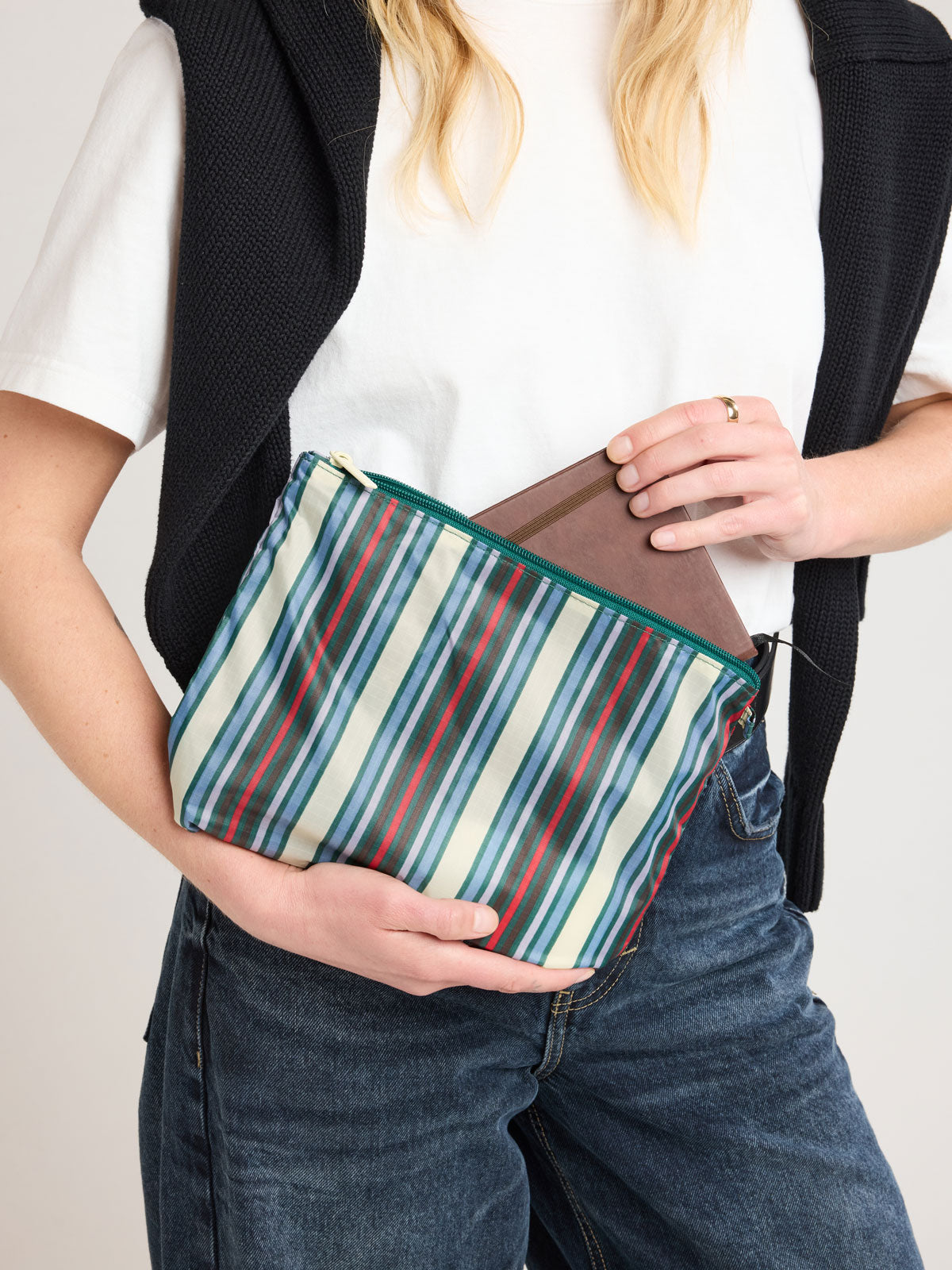 Person adding item in CALPAK Compakt ZIppered Pouch Set in multicolor stripes; KZB2001-RIVIERA-STRIPE