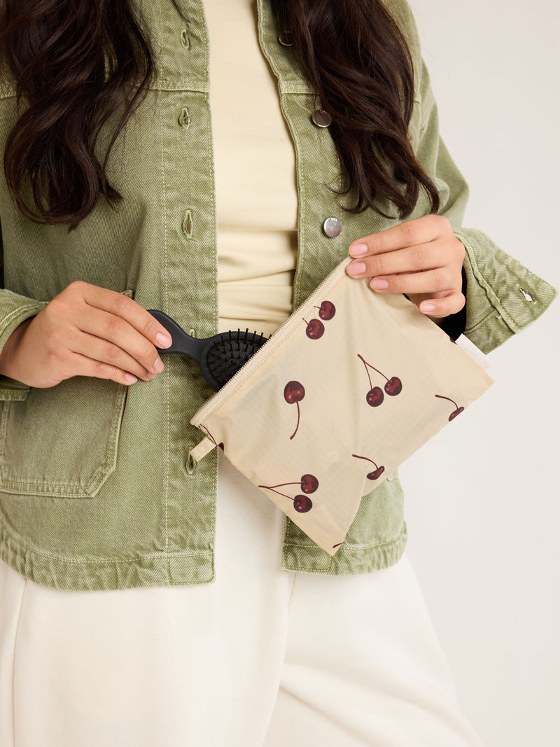 Model holding CALPAK  Compakt Zippered Pouch in beige with cherry pattern