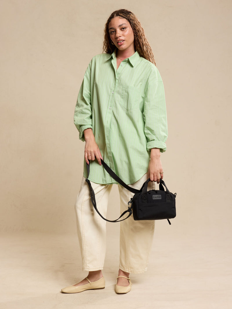 CALPAK Connect Crossbody Bag with adjustable strap in beige Black being held by a woman against a beige background