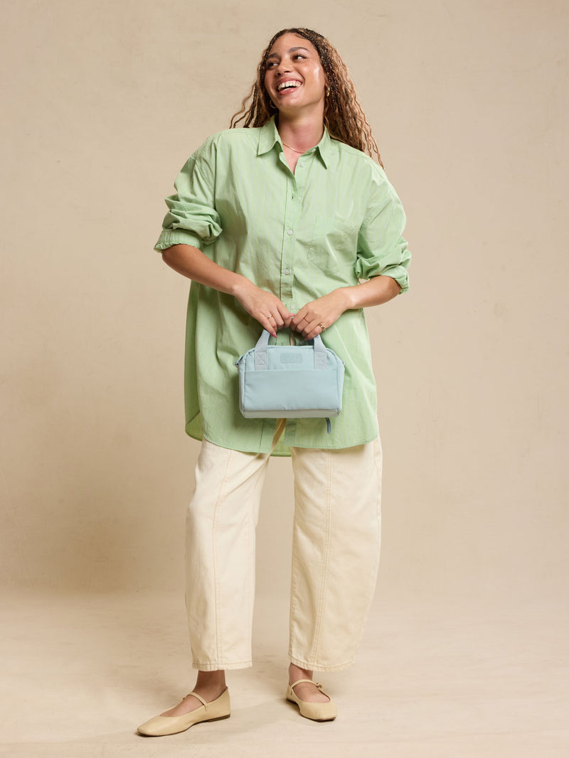 CALPAK Connect Crossbody Bag with adjustable strap in light blue Bluebell being held by a woman against a beige background