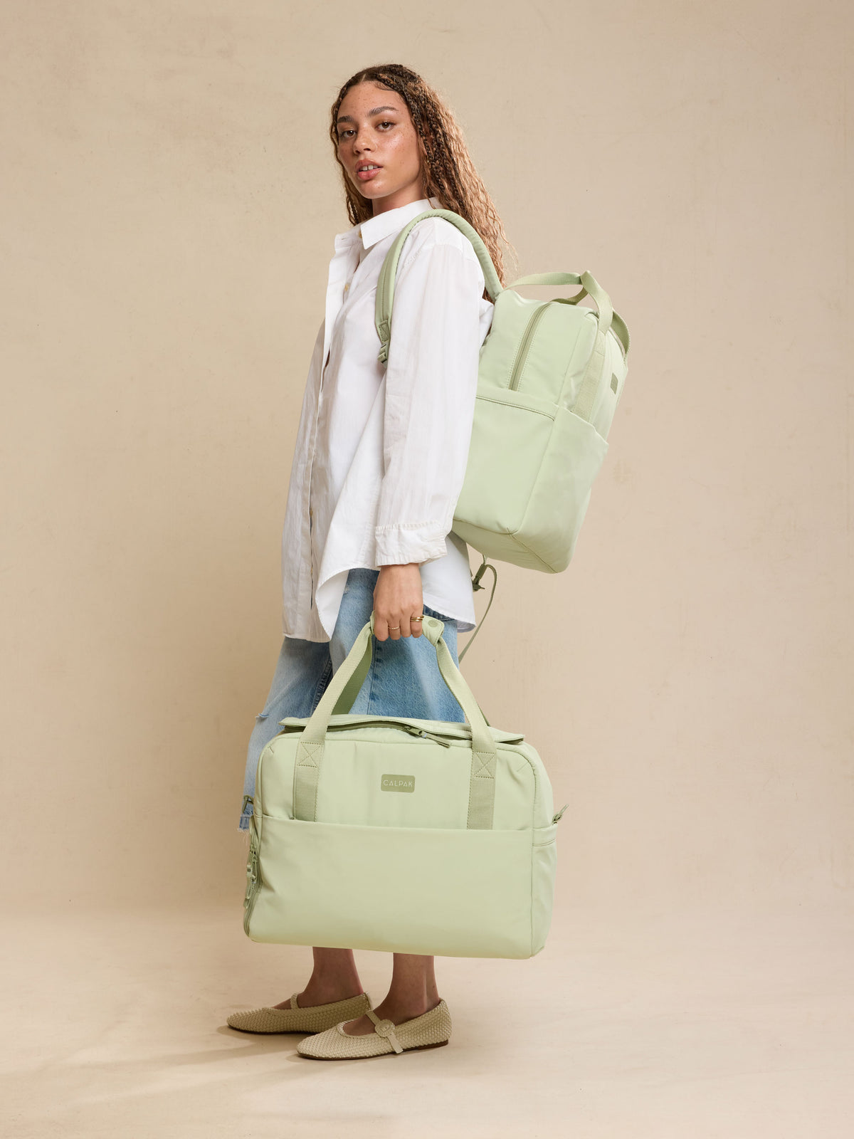 Model holding the CALPAK Laptop Duffel in light green Meadow with beige  background; DCN2401-MEADOW