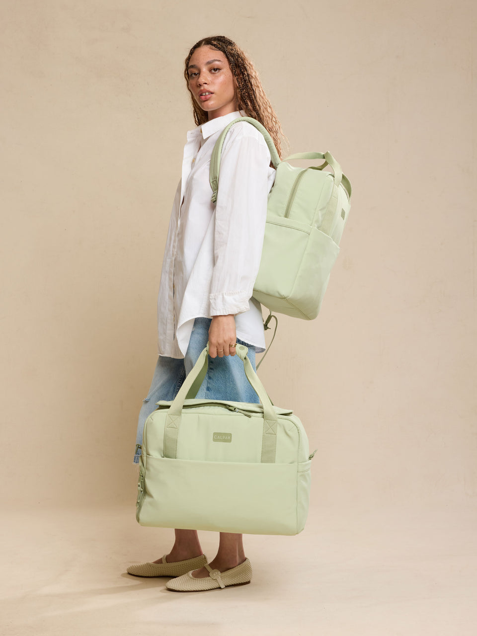 Model holding the CALPAK Laptop Duffel in light green Meadow with beige  background; DCN2401-MEADOW