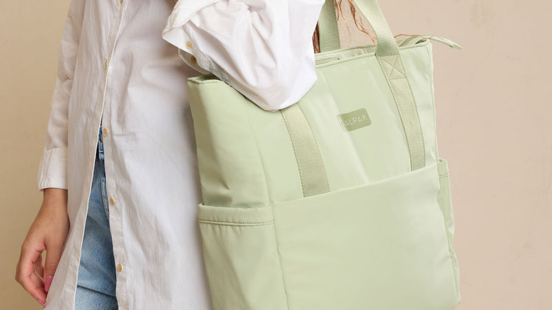 CALPAK Connect Zippered Laptop Tote in light green Meadow being worn by model against a beige background