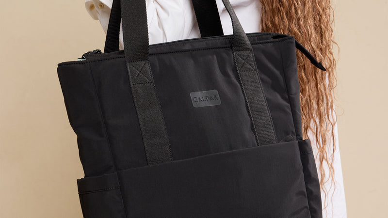 CALPAK Connect Zippered Laptop Tote in Black being worn by model against a beige background